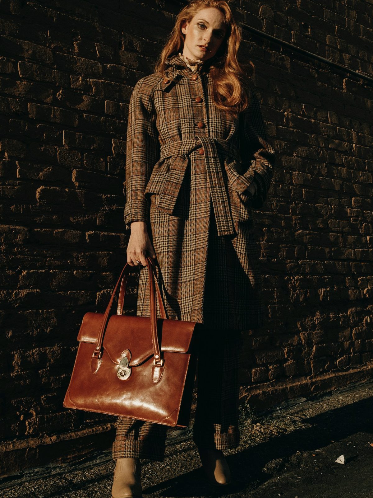 A woman in a check trench coat holding a cognac leather bag