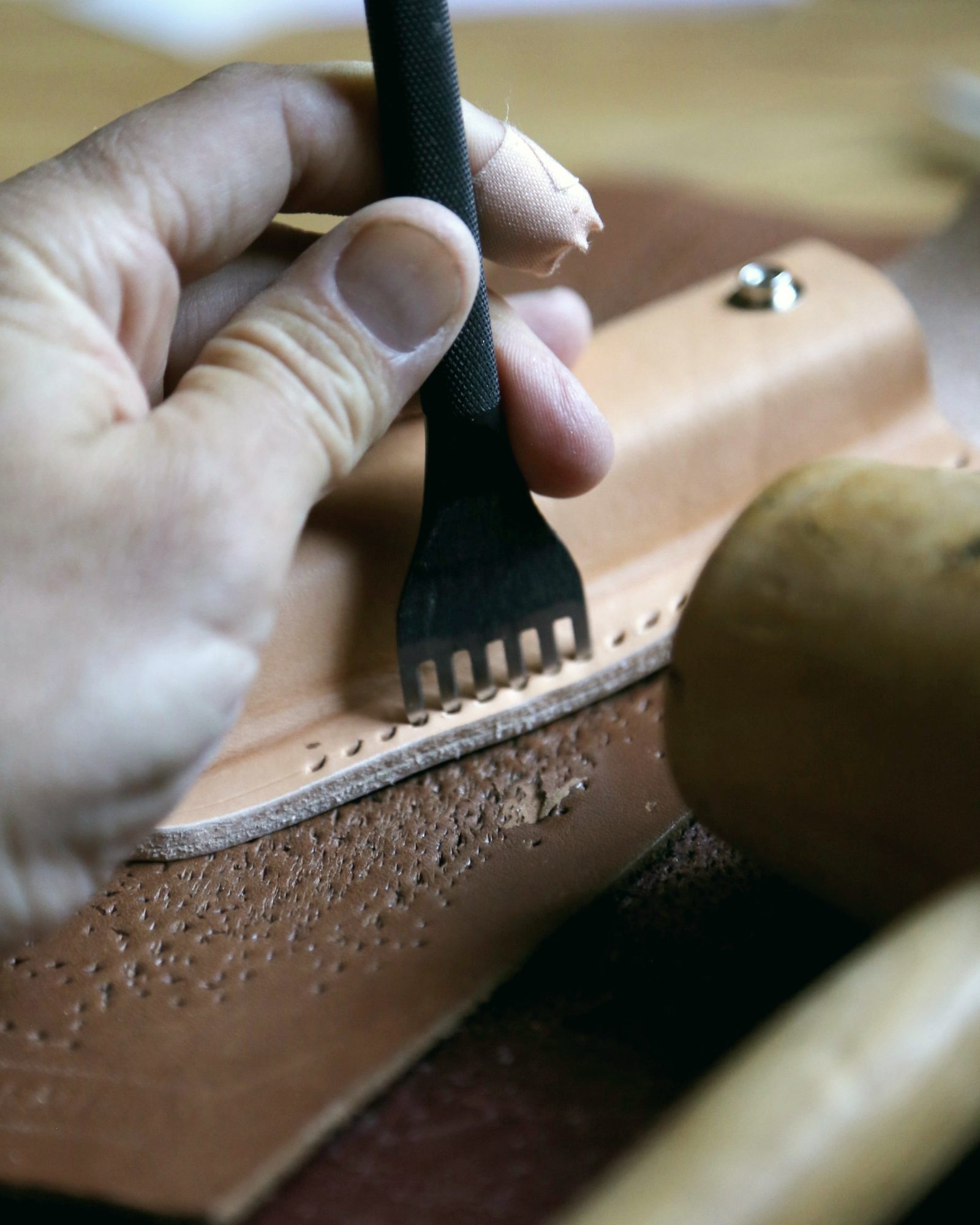 Artisan marking stitch holes along a leather edge with a pricking iron