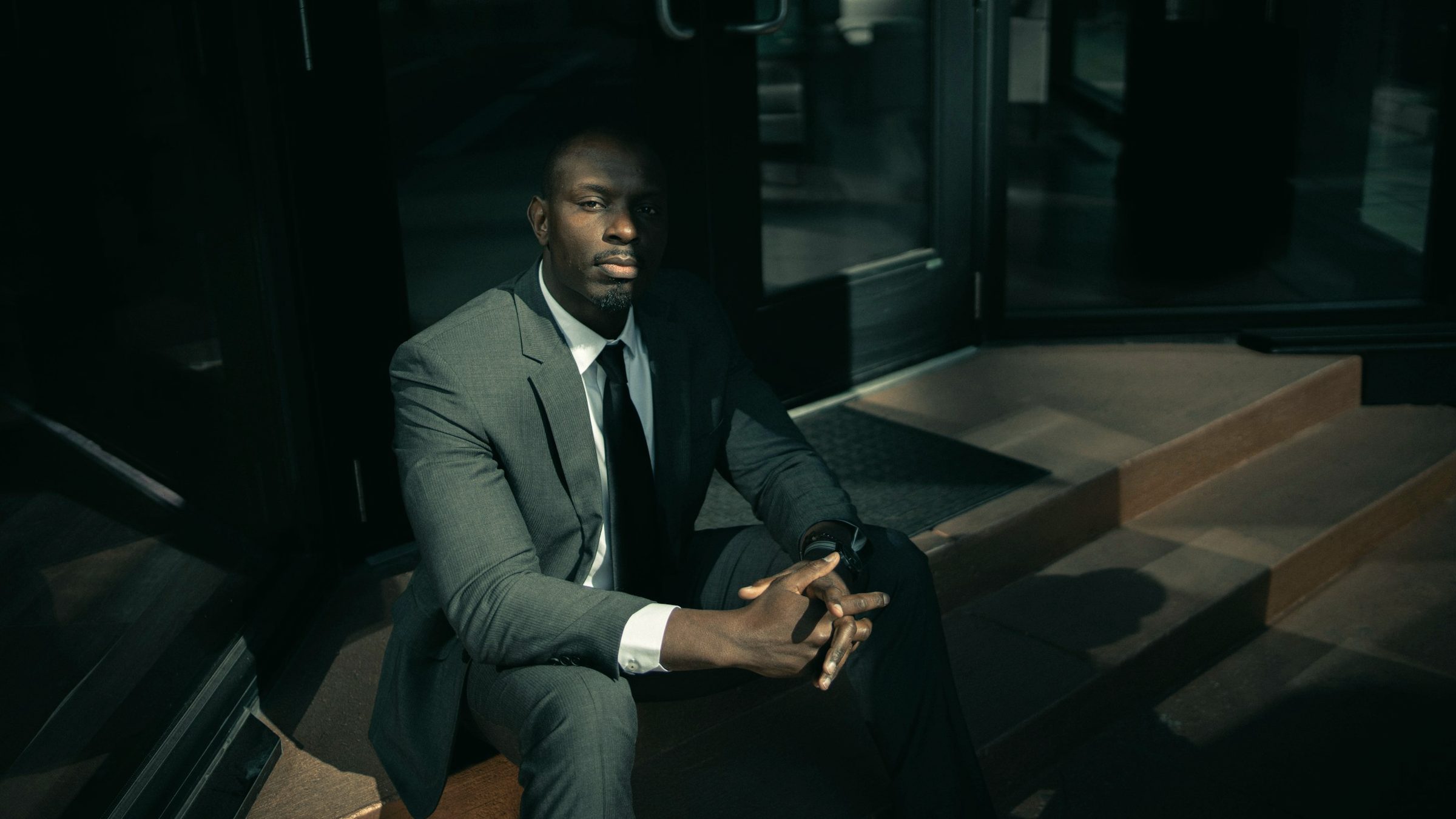 A man in a dark tailored suit seated in a moody interior