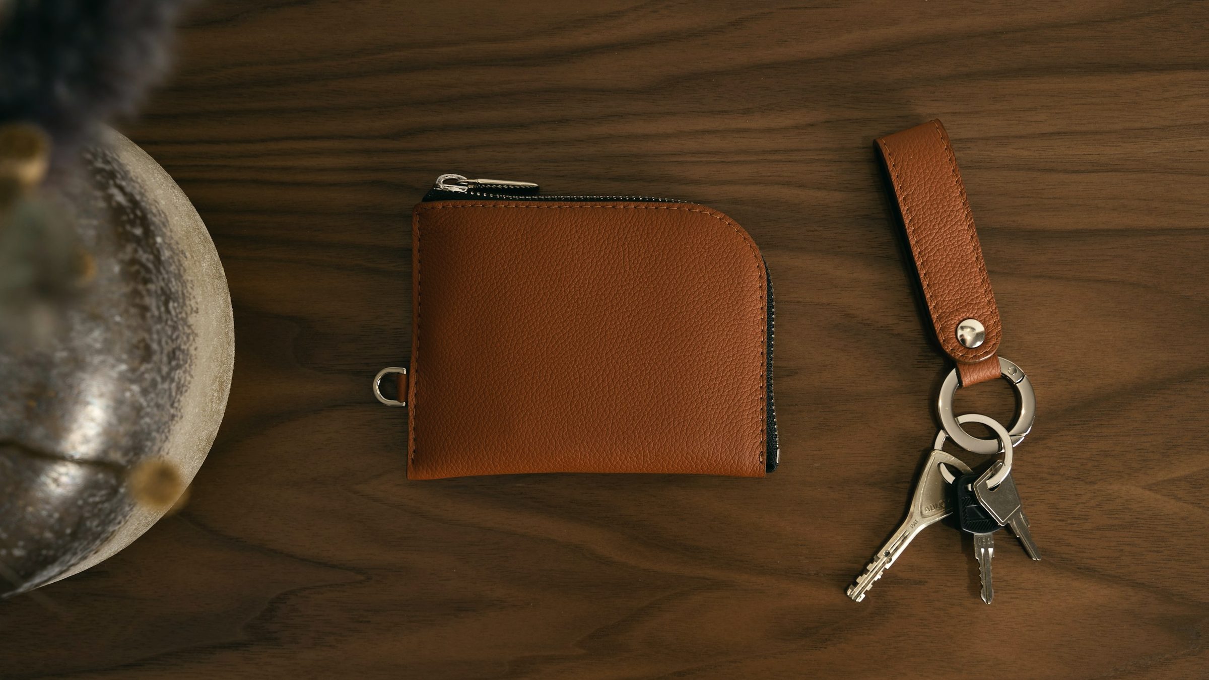 A cognac leather wallet and key fob on a walnut table