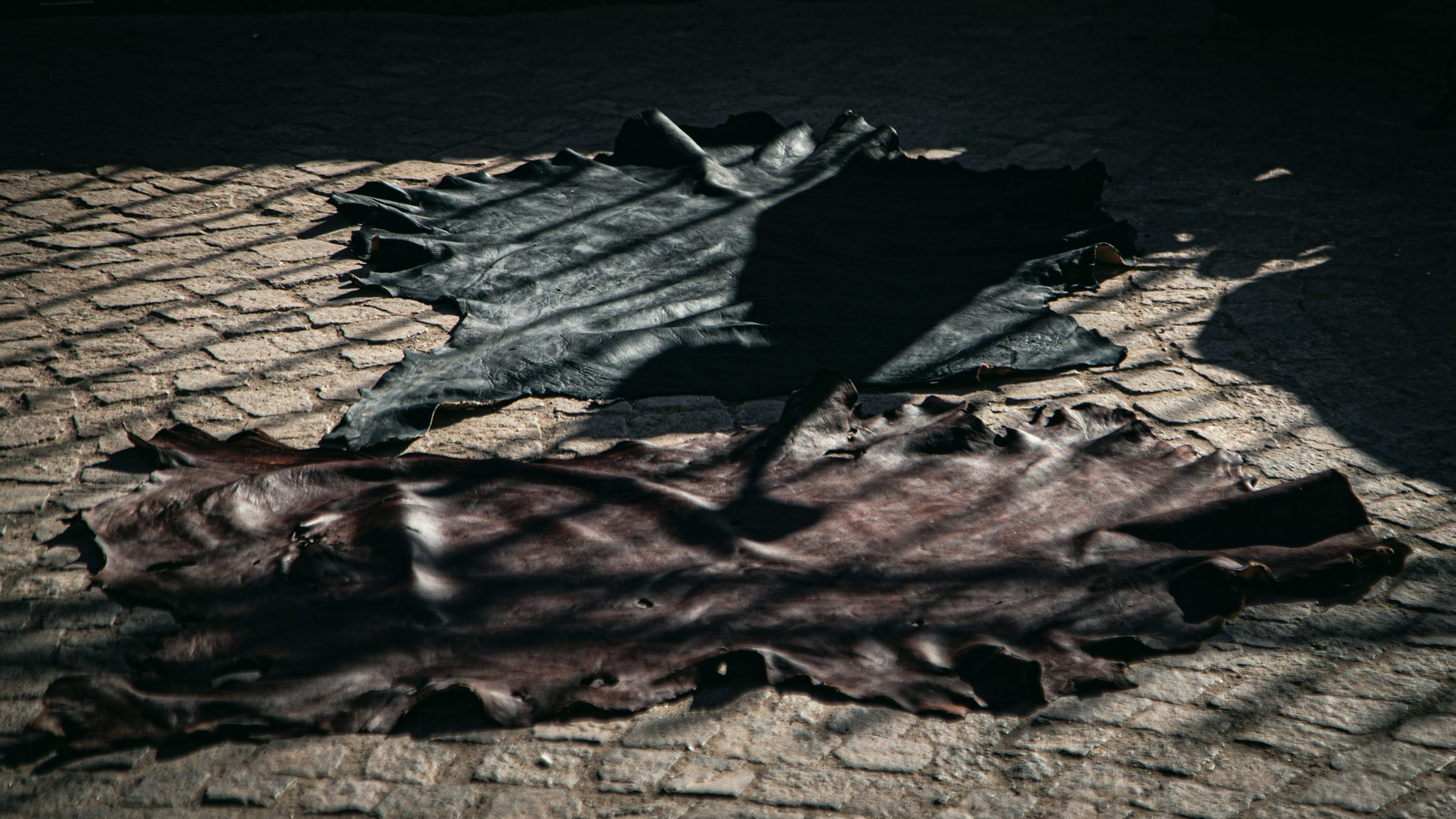 Raw leather hides laid out on dark cobblestones