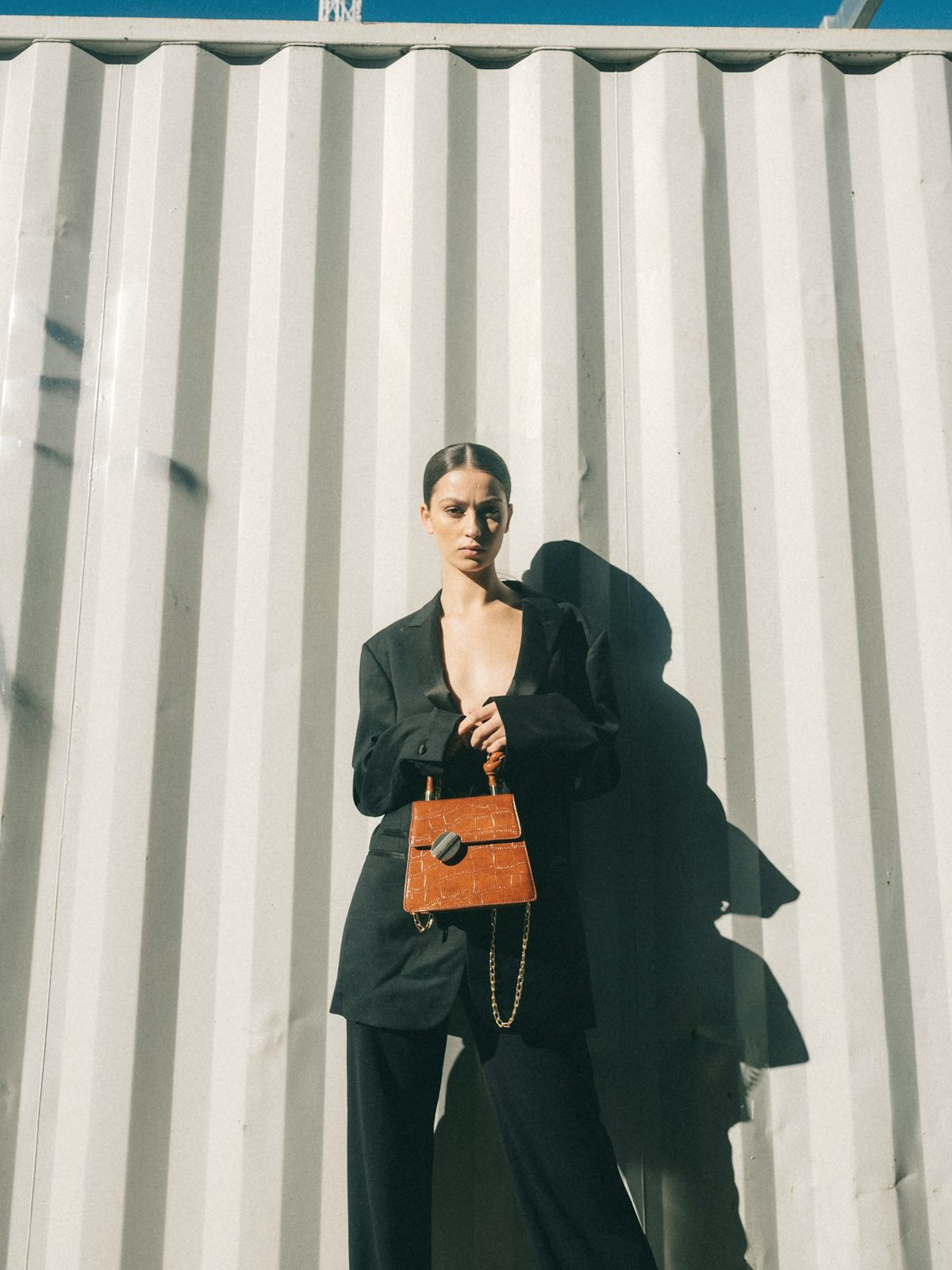 A woman in a dark suit holding a small cognac handbag