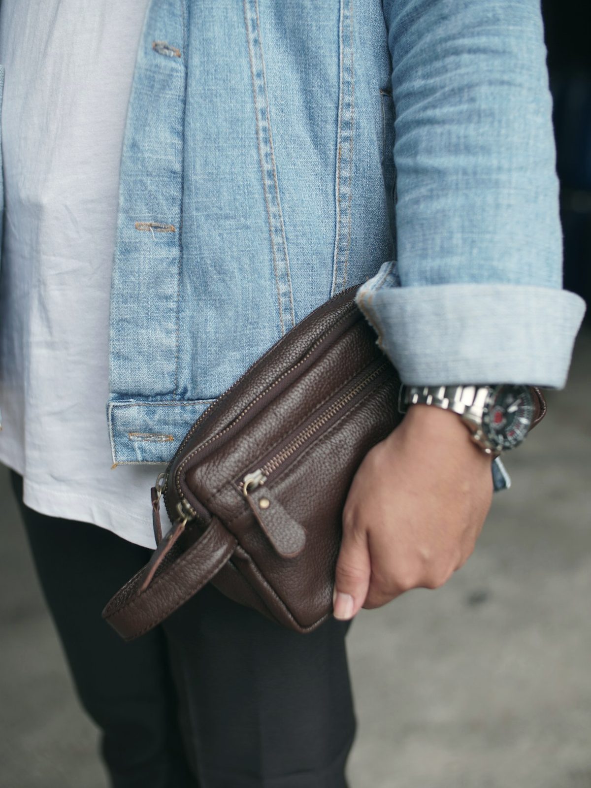 A man in a denim shirt holding a brown leather clutch