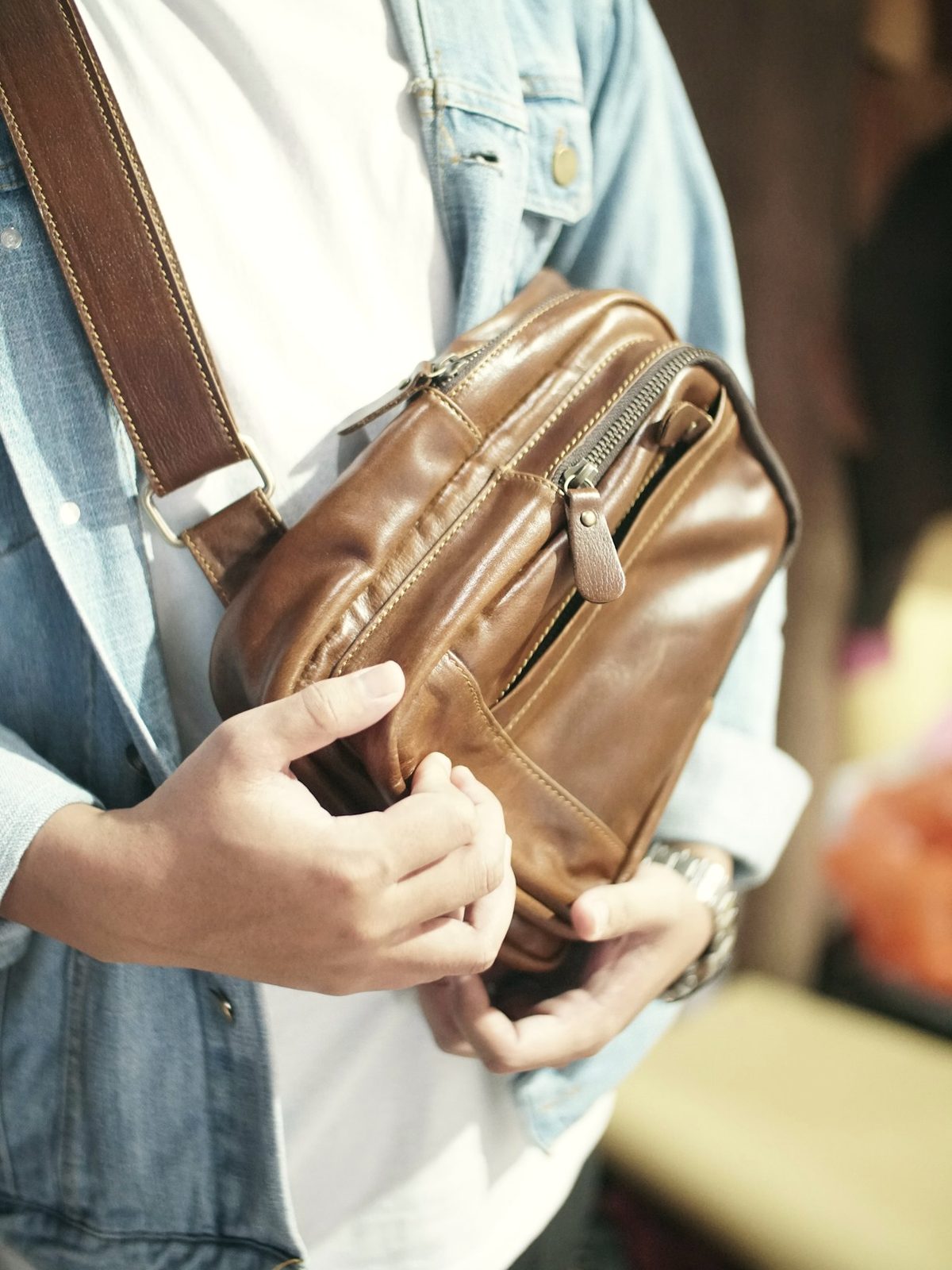 A man wearing a tan leather crossbody bag over a denim jacket