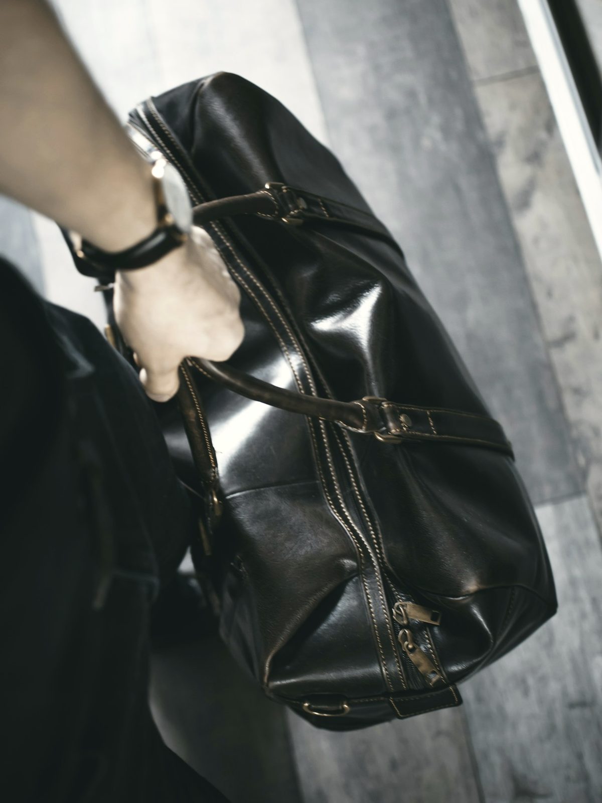 A hand carrying a black leather duffel bag